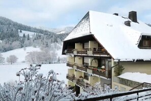 A multi-story chalet with balconies, surrounded by snow-covered landscape and mountains.
