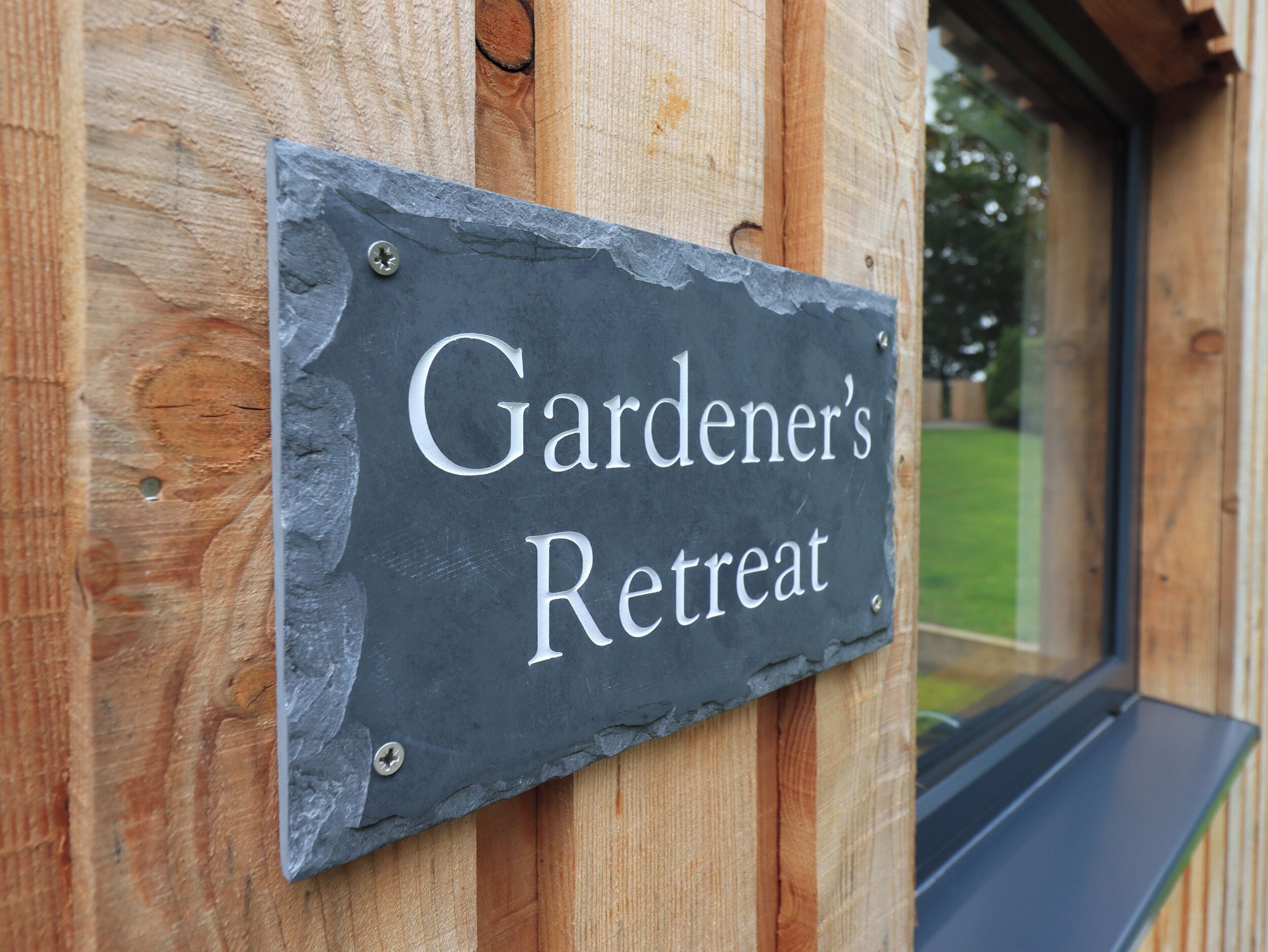 Un letrero de pizarra con el texto 'Gardener's Retreat' colocado sobre un poste de madera.
