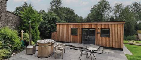 A wooden cabin with a patio area, including a hot tub, seating, and a table.