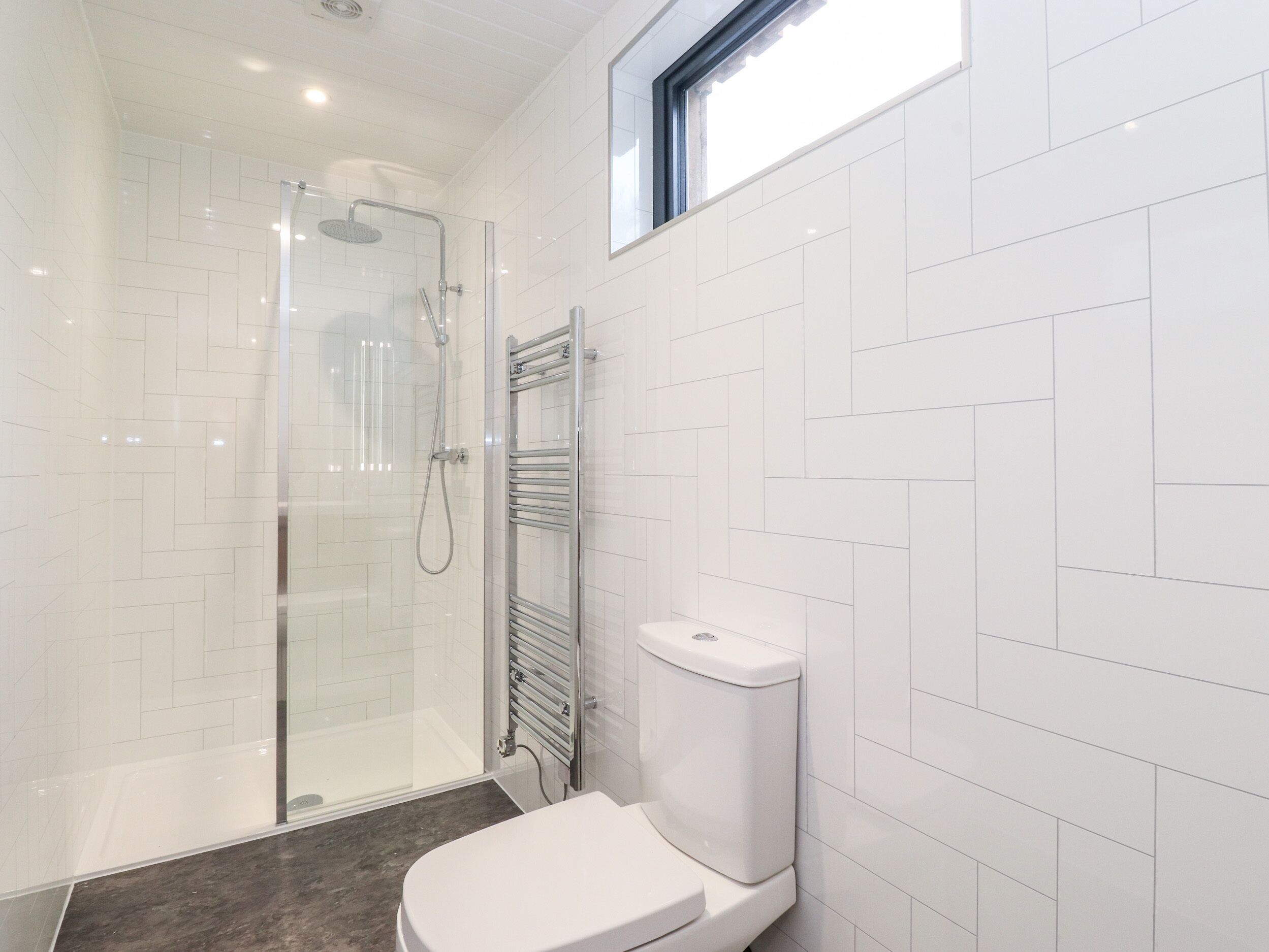 Une salle de bain moderne avec une douche à parois de verre, des toilettes blanches et un porte-serviettes.