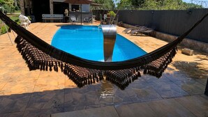 Una hamaca sobre una piscina con zona de patio, mobiliario exterior y un edificio con techo de tejas.