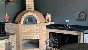 Una cocina con horno de ladrillo, encimeras de granito, un fregadero y una zona de comedor con una mesa redonda y sillas de metal.