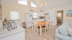 A spacious kitchen with white cabinets, a wooden dining table, and a chandelier. - Vitamin Sea, Almost Oceanfront House in Emerald Isle, NC! (Emerald Isle)