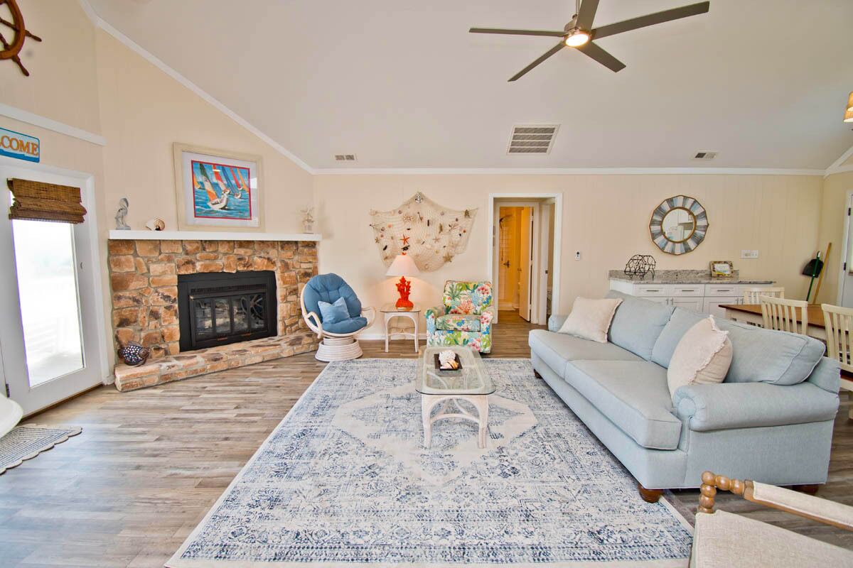A living room with a stone fireplace, a blue armchair, a light blue sofa, and a ceiling fan.