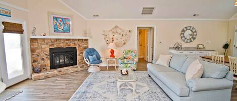 A living room with a stone fireplace, a blue armchair, a light blue sofa, and a ceiling fan.