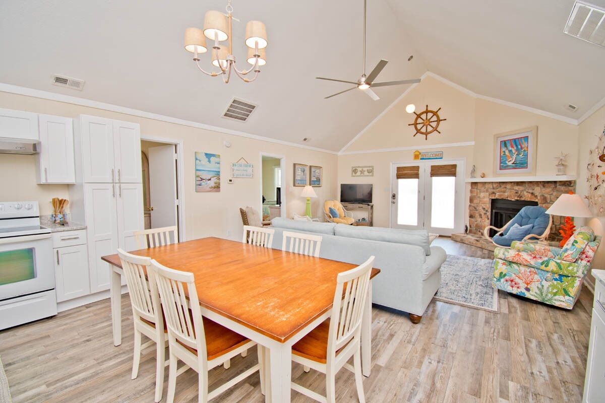 A spacious living area with a wooden dining table, white chairs, a light blue sofa, a colorful armchair, and a fireplace.