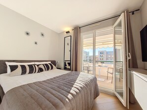 A bedroom with a bed, a large mirror, and a sliding glass door leading to a balcony. - N&J - PERLE DOREE - Terrace - Design (Niza)