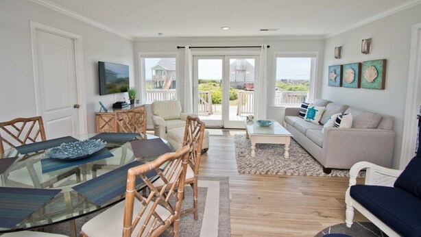 A spacious living room with a glass dining table, comfortable seating, a sofa, and a view through large sliding doors to the outdoors.
