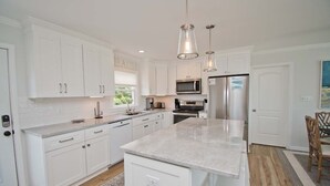 A modern kitchen with white cabinetry, stainless steel appliances, and pendant lighting.
