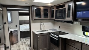 Une cuisine compacte pour camping-car, équipée d’une cuisinière, d’un évier, d’un four à micro-ondes et d’un petit coin repas.