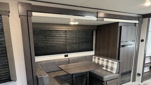 Un intérieur de camping-car compact comprenant un coin cuisine, un espace repas et un coin salon avec une banquette et une table.