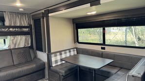 Un intérieur de camping-car compact comprenant un coin cuisine, un espace repas et un coin nuit.