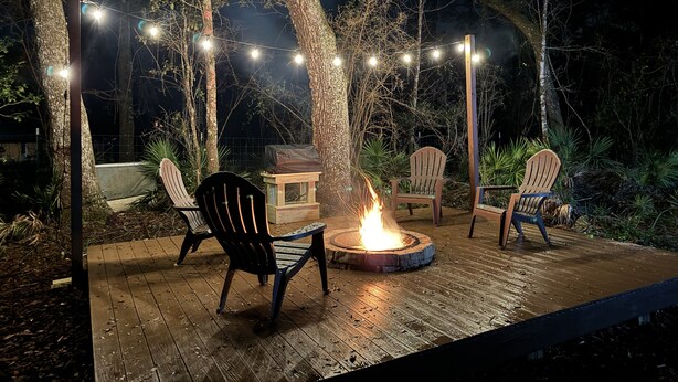Une terrasse extérieure avec des chaises en bois, un foyer et des guirlandes lumineuses.