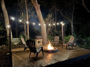 Una terraza al aire libre con sillas de madera, un brasero y luces colgantes.