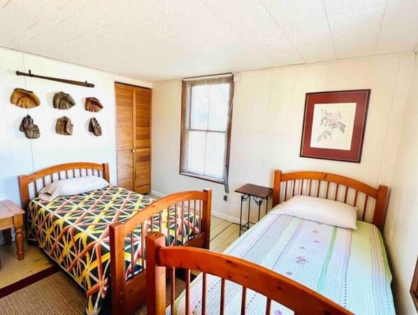 A room with two wooden beds, a wooden wardrobe, a small table, and a window with blinds. - The Addison House est. 1865 (Addison)