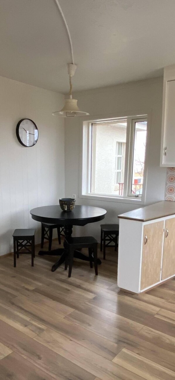 Une pièce comprenant une table de salle à manger ronde, deux tabourets, un meuble blanc et une fenêtre donnant sur un paysage agréable.