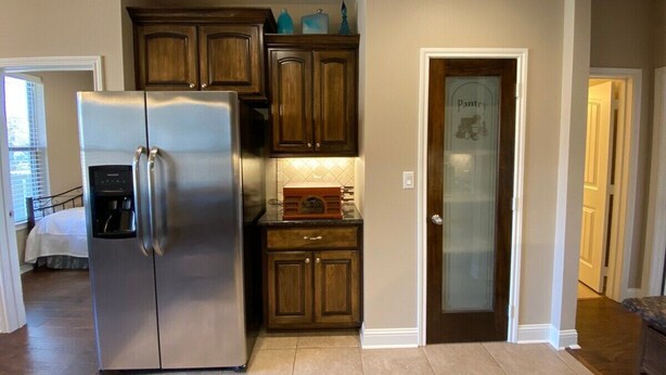 A kitchen with a stainless steel refrigerator, wooden cabinets, a built-in oven, and a pantry door.