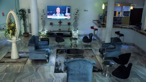 A modern lobby with a TV displaying a news channel, seating arrangements, and a bar area. - Golden Tulip Hotel GT31-Rivotel (Port Harcourt)