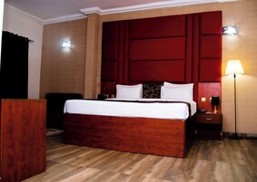 Una habitación de hotel con una cama grande, una mesita de noche, una lámpara y suelo de madera.