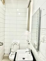 Un baño pequeño y moderno con azulejos blancos, un lavamanos blanco, un inodoro y un espejo.