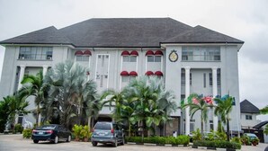 A large, white building with a grey roof, multiple windows, and a flag on the right side. - Golden Tulip Hotel GT31-Rivotel (Port Harcourt)