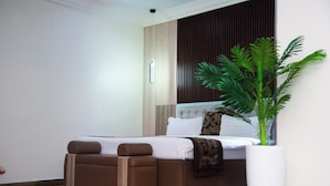A modern bedroom with a bed, two brown ottomans, a large potted plant, and a white vase. - Golden Tulip Hotel GT31-Rivotel (Port Harcourt)