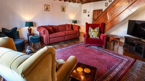 A cozy living room with a red sofa, a plush armchair, and a television. A wooden staircase leads to an upper level. - Old Roost Farmhouse (York)
