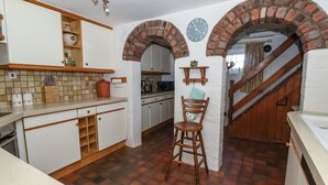 A kitchen with white cabinets, a wooden stool, and a brick archway. - Old Roost Farmhouse (York)