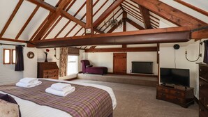 Ein Schlafzimmer mit einem großen Bett, einem Fernseher, einem Schminktisch und einem Fenster mit Vorhängen.