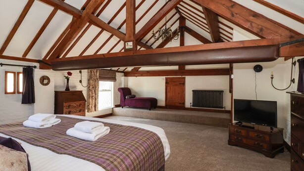 A bedroom with a large bed, a television, a dresser, and a window with curtains. - Old Roost Farmhouse (York)