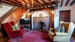A cozy living room with a fireplace, red and beige armchairs, a TV, and a patterned rug. - Old Roost Farmhouse (York)