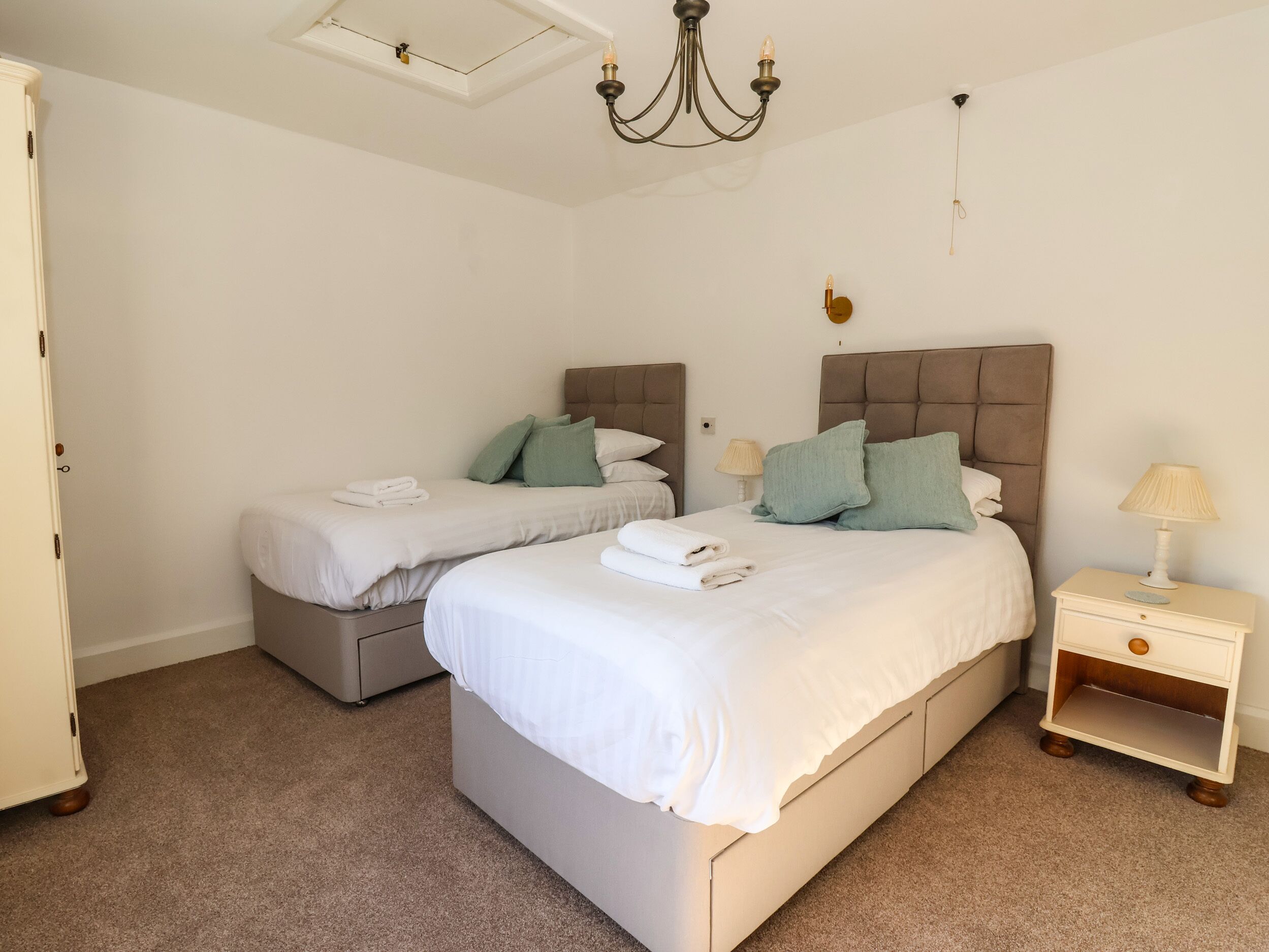 A bedroom with two beds, a chandelier, bedside lamps, and a nightstand.