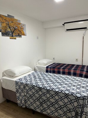 A small, clean room with two single beds, a wall-mounted air conditioner, and a framed picture of trees. - CABANA ALVORADA (Balneário Camboriú)