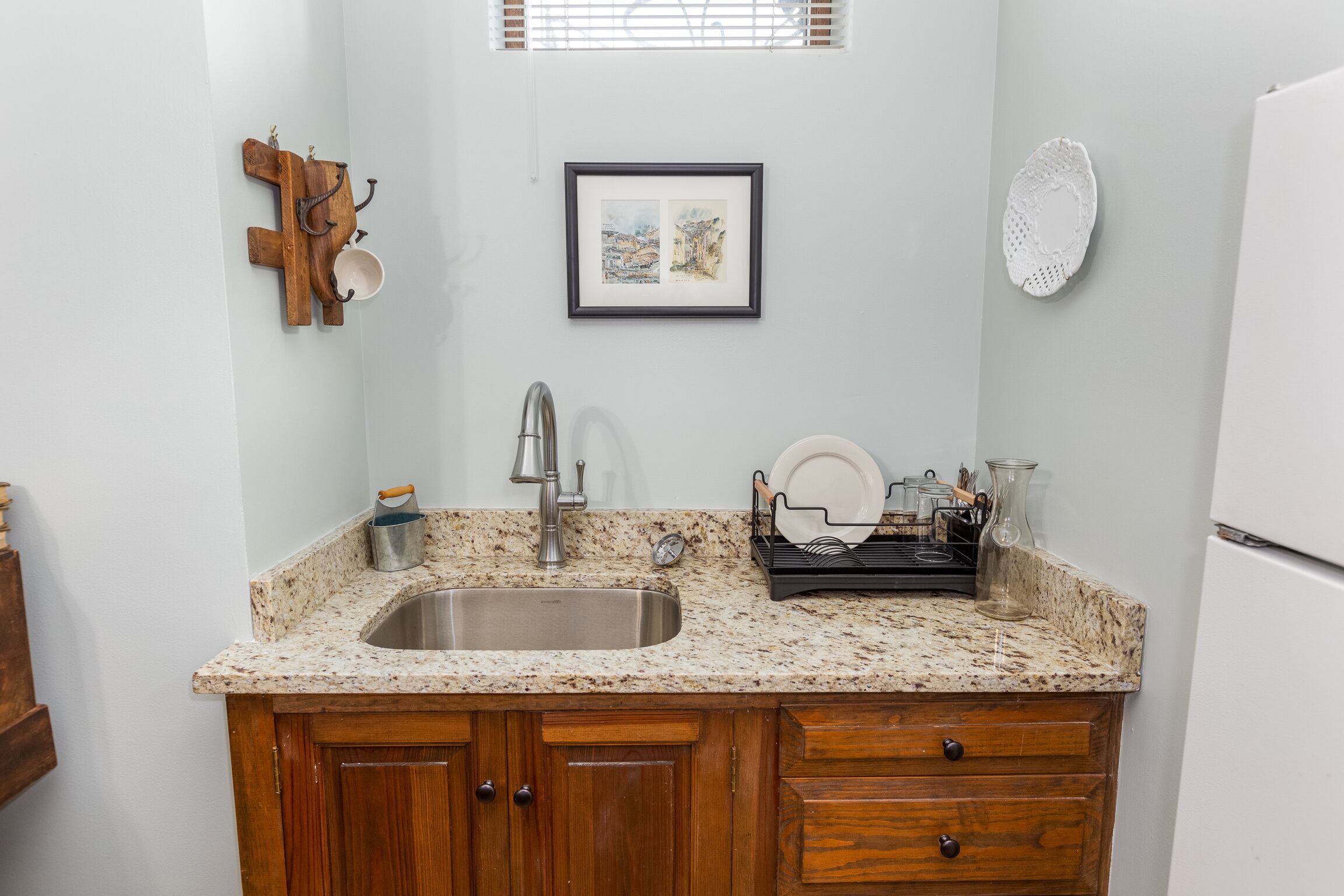 A kitchen with a granite countertop, wooden cabinets, a stainless steel sink, and a hanging light fixture.