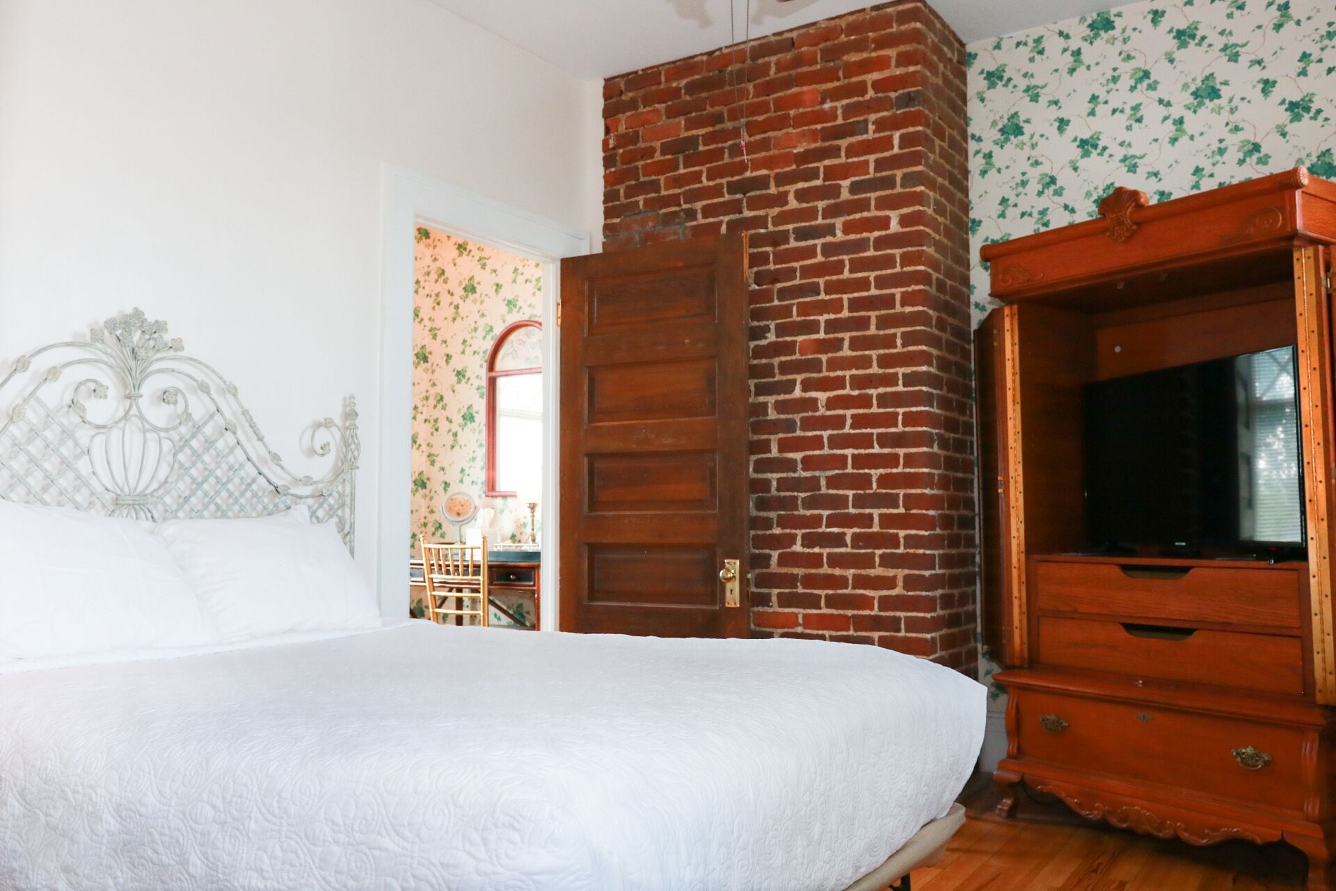 A bedroom with a bed, a wooden dresser, a brick wall, and a mirror.