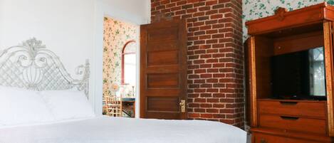 A bedroom with a bed, a wooden dresser, a brick wall, and a mirror.