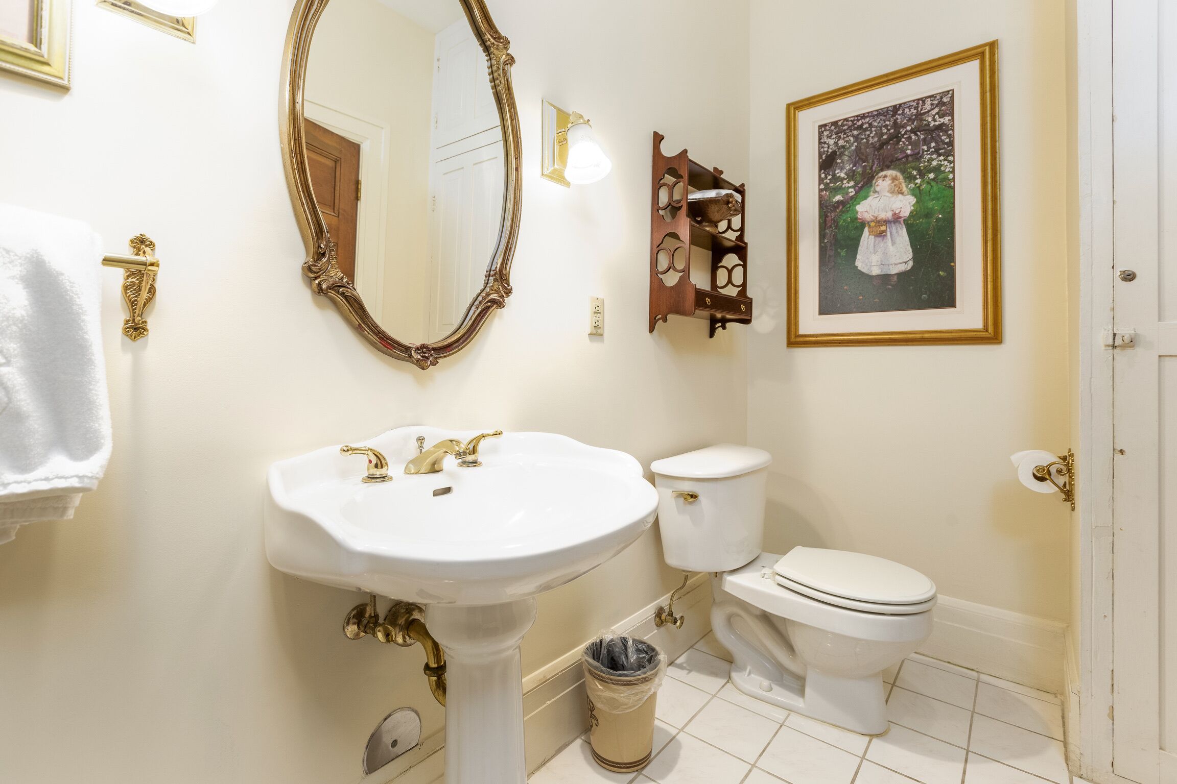 Un baño con lavamanos pedestal, inodoro, espejo grande y un cuadro en la pared.