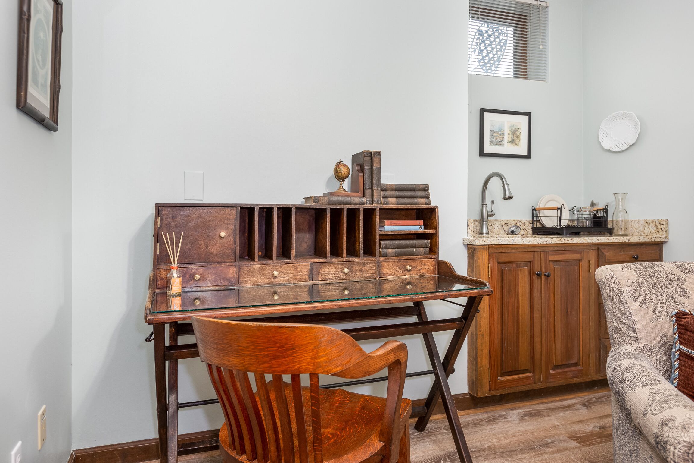 A compact kitchen with wooden cabinetry, a glass-top table, and a patterned armchair.