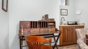 A compact kitchen with wooden cabinetry, a glass-top table, and a patterned armchair.