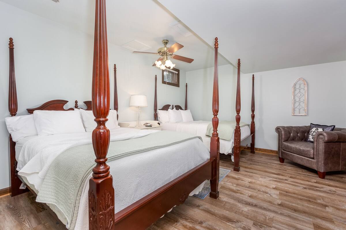 A four-poster bed with a ceiling fan, a brown leather sofa, and a wooden floor.