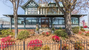 A Victorian-style house with a prominent front porch, large windows, and a well-maintained garden with flowering plants. - The Shaffner Inn (Winston-Salem)
