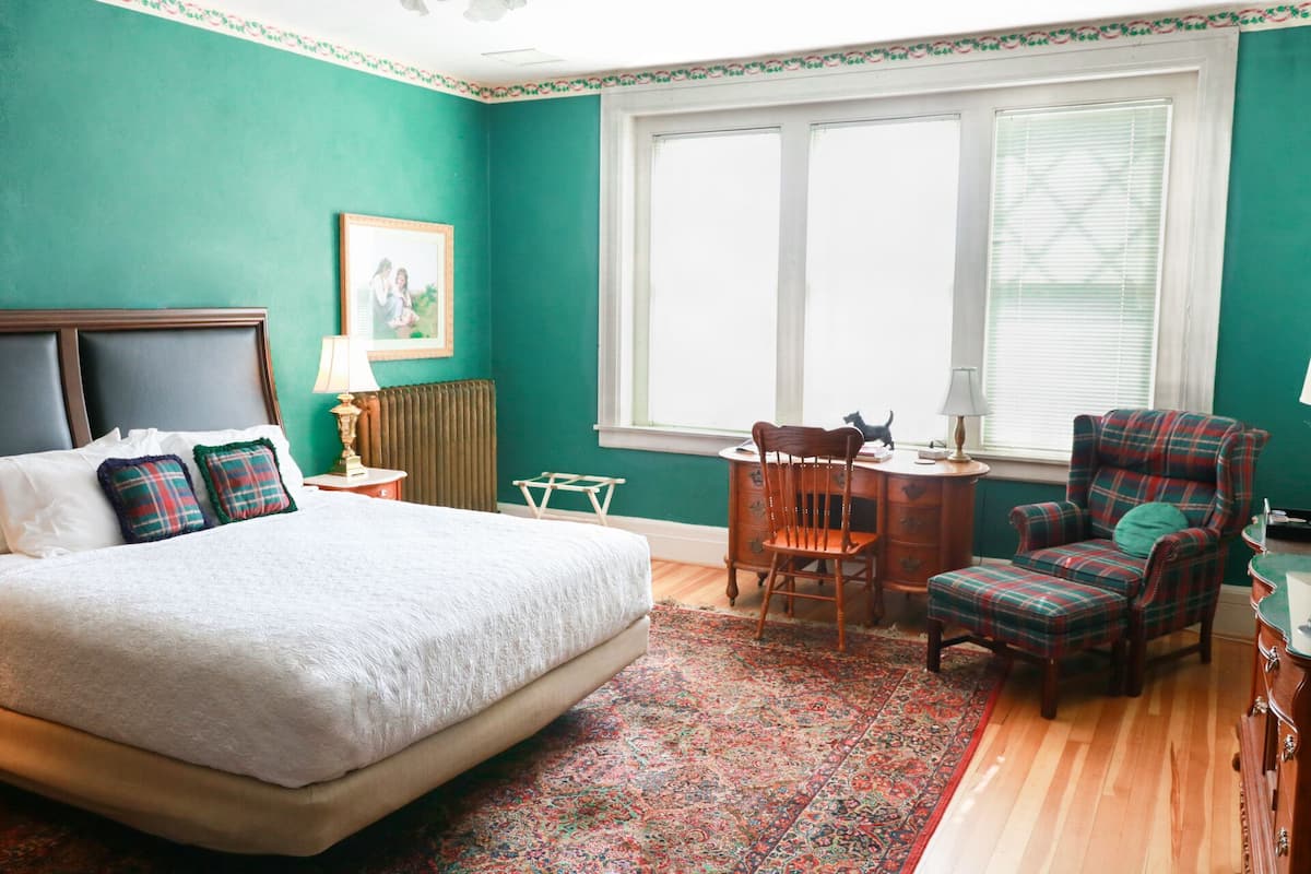 A bedroom with a bed, a chair, a desk, and a window.