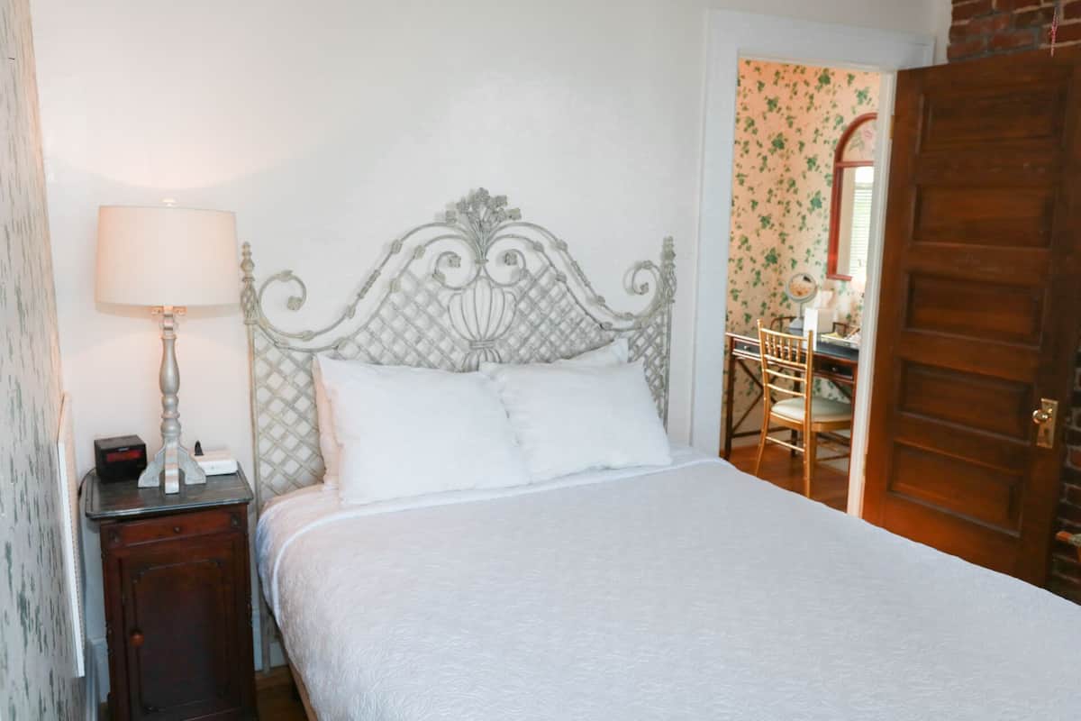 A neatly made bed with a white comforter and pillows, a bedside table with a lamp, and a wooden door.