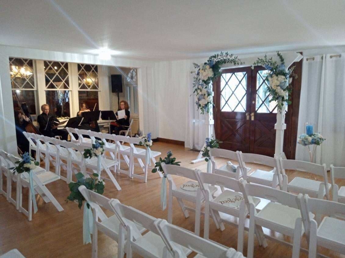 A room with white chairs arranged in rows, a piano, and a decorative floral arrangement near the door.
