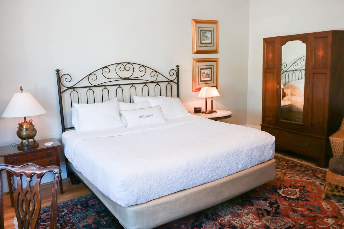 A neatly made bed with white linens, a metal headboard, two bedside tables with lamps, and a large mirror cabinet.
