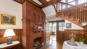 A room with a brick fireplace, wooden staircase, and a table with a lamp. - The Shaffner Inn (Winston-Salem)