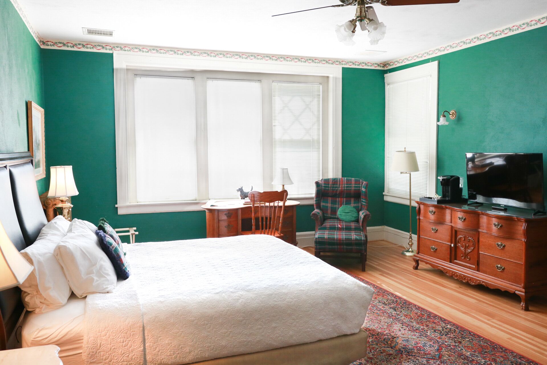 A bedroom with a bed, a desk, a chair, a dresser, and a television.