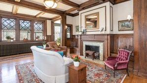 A traditional living room with a fireplace, wooden beams, and a large mirror. - The Shaffner Inn (Winston-Salem)