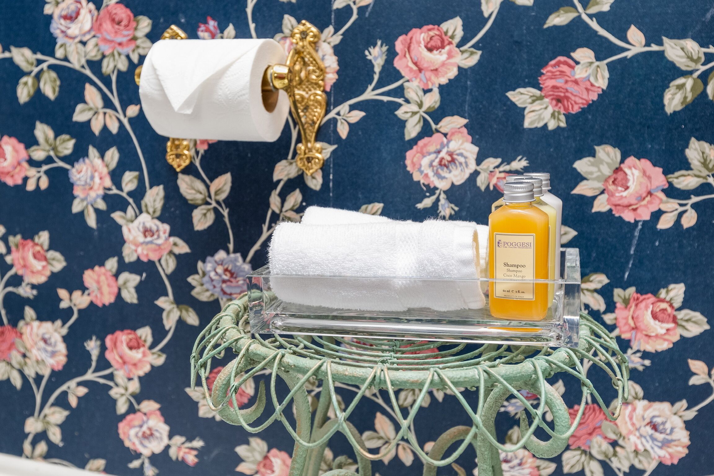 Un baño con papel tapiz floral, un dispensador de papel higiénico, una toalla y una botella de champú.