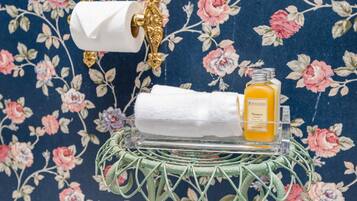 Un baño con papel tapiz floral, un dispensador de papel higiénico, una toalla y una botella de champú.